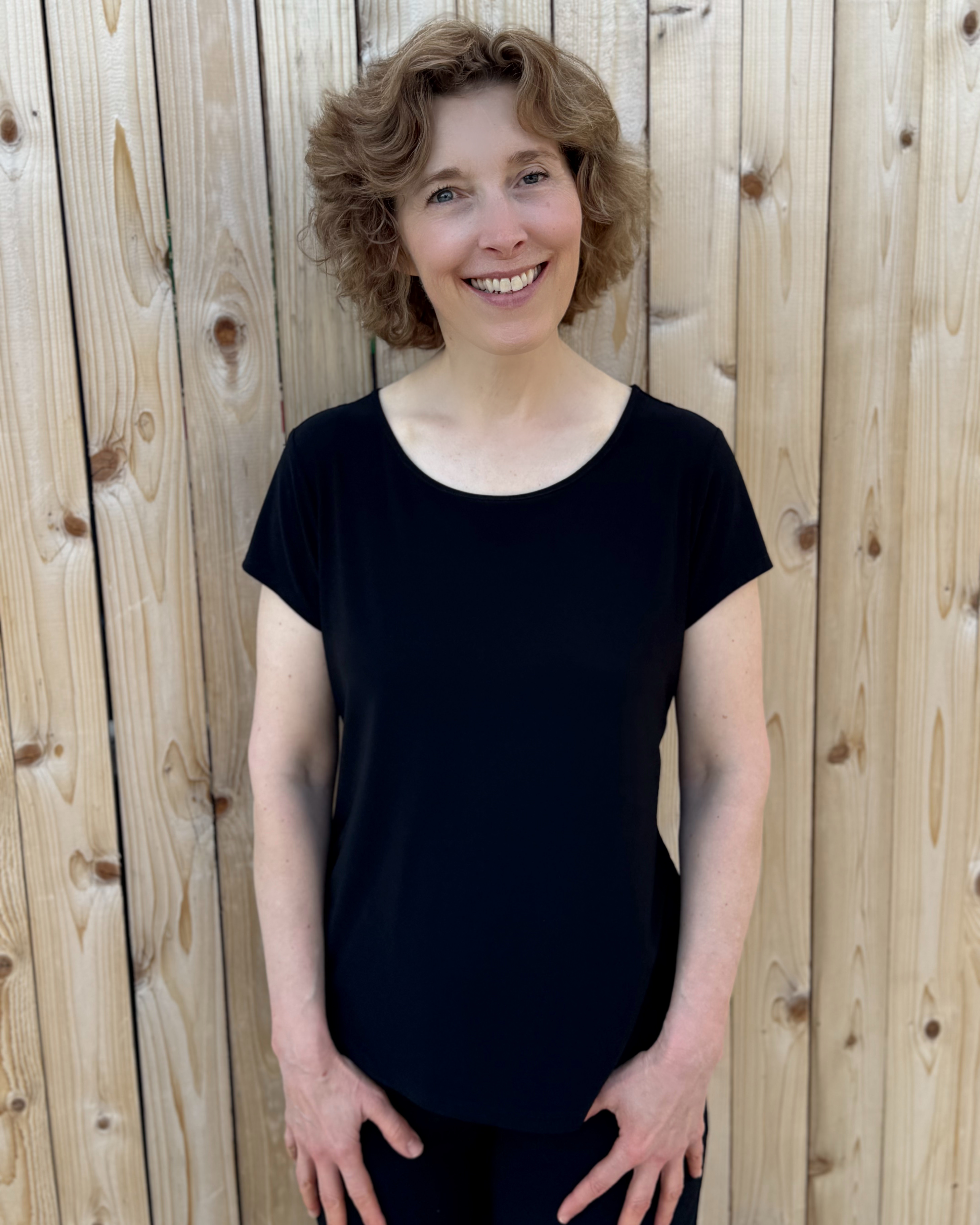 Kim smiling in a black shirt standing in front of a wood fence.
